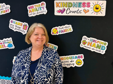 teacher with blonde hair smiling in front of board